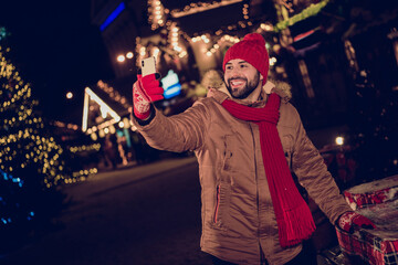 Photo of funny cheerful guy dressed coat recording video x-mas vlog modern device outdoors urban...