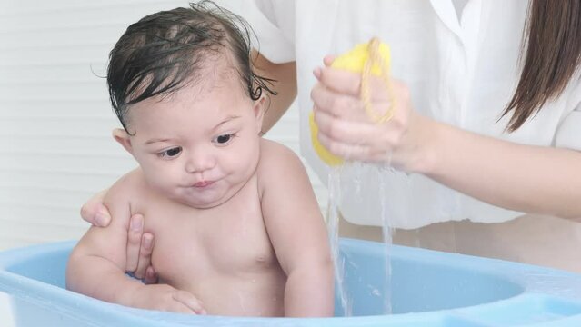 Adorable little girl having fun splashing in the blue bathtub while mom gives her a bath.