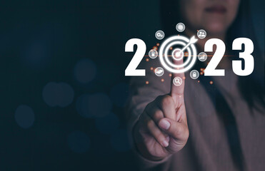 Businesswoman's finger pressing starting up 2023 button on virtual interface on black background with copy space for text. New year, new job, start up business. Beginning of New Year 2023 concept.