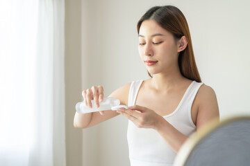 Making beauty routine, attractive asian young woman hand holding cotton pad and bottle, female applying facial wipe on her face remover washing makeup, essence or lotion of skin care treatment at home