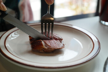 Cutting a piece of steak with a knife on a white plate