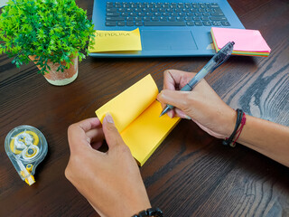women write in yellow notes, mock up yellow notes. Women's hands write notes on yellow note paper in the background of the office desk workspace from the top view.