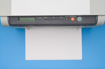 Top view of an office printer and a blank sheet of paper on a blue background.