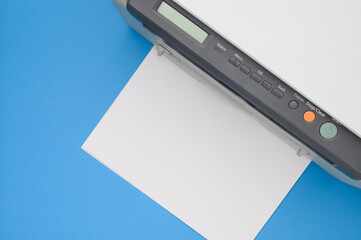 Top view of an office printer and a blank sheet of paper on a blue background.