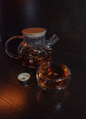 Warm teapot of black tea with a glass cup with a candle.