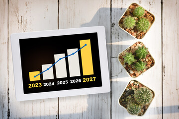 Green technology business with five years forecast on computer tablet with cactus on desk...