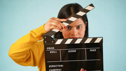 Closeup of a beautiful young Asian Indian woman standing holding clapperboard, clapper board used...