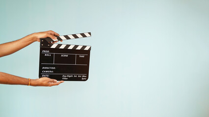Hand is holding clapper board or clapperboard or movie slate, used in film production and cinema ,movies industry isolated over blue background. - obrazy, fototapety, plakaty