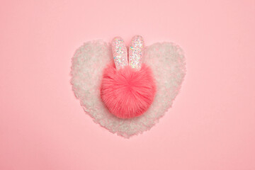Fluffy pompom with cute ears on artificial snow in the shape of a heart. Christmas concept.