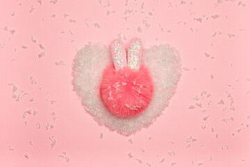 Fluffy pompom with cute ears on artificial snow in the shape of a heart. Christmas concept.
