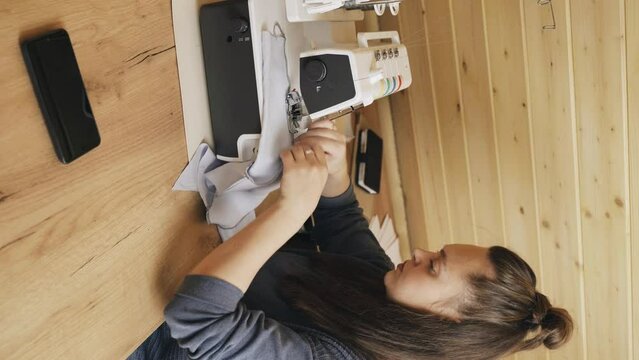 A woman designer works on an overlock sewing machine on tailoring. Vertical frame. Small tailoring business.