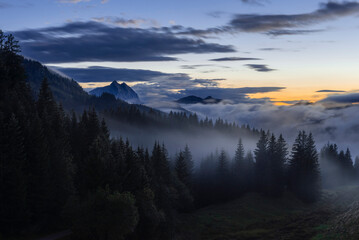 Fototapeta na wymiar Nebelschwaden ziehen nach einem Sommergewitter in der Abenddämmerung durch die Bergwälder an der Ackernalm, Tirol, Österreich