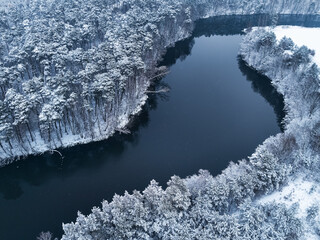 Flying above forest with snow and river in winter, Poland.