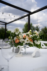Table centerpiece with white and peach rustic floral arrangement in glass vase. Rustic wedding table.