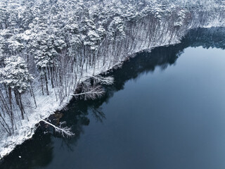 Flying above snowy forest and small river in winter, Poland.