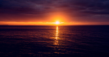 Sunset over the Beagle Channel in Argentina.  Image Has a sliver of sunlight due to the storm clouds, and there is a faint silhouette of land. 