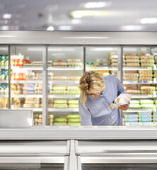  Man choosing frozen food from a supermarket freezer., reading product information