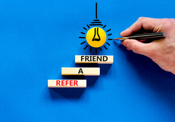 Refer a friend symbol. Concept words Refer a friend on wooden blocks on a beautiful blue table blue...