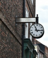  the  public white  clock  hang on bronze silver sign and  dirt  brick wall  at Minster gate York  UK. vintage public clock