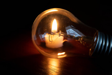 light bulb and candle on black background, blackout	