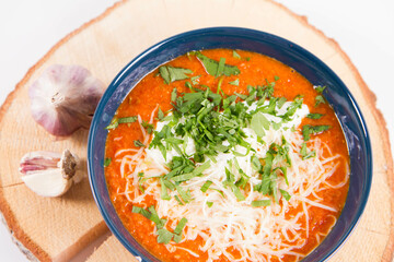 Italian tomato soup served with cream, mozzarella cheese and fresh parsley in a bowl, on a wooden pad decorated with garlic	
