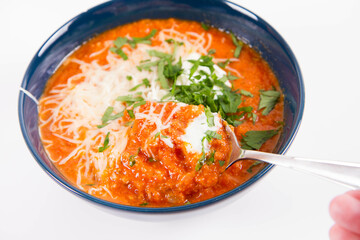 Italian tomato soup served with cream, mozzarella cheese and fresh parsley in a bowl, eaten with a spoon	
