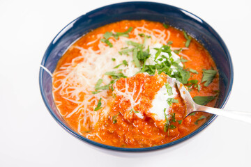 Italian tomato soup served with cream, mozzarella cheese and fresh parsley in a bowl, eaten with a spoon	
