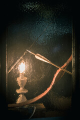 a candle in a candlestick burns behind a frozen window, an energy crisis