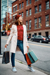 Full length of happy Asian woman with shopping bags on city street.