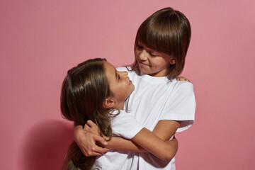 Smiling little girls hug and look at each other