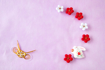 日本の正月イメージ　干支の卯年の人形と紅白のちり緬の梅と水引のデザイン(ピンクの和紙の背景）