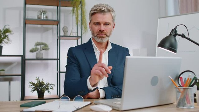 Mature businessman working on laptop computer shakes finger and saying No be careful scolding and giving advice to avoid danger mistake disapproval sign at office. Confident freelancer middle aged man