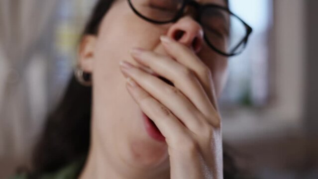 Pretty Young Caucasian Sleepy Woman With Glasses Is Working At Laptop And Yawning In Close-up. Zoom In And Out. Concept Of Overwork And Boredom.