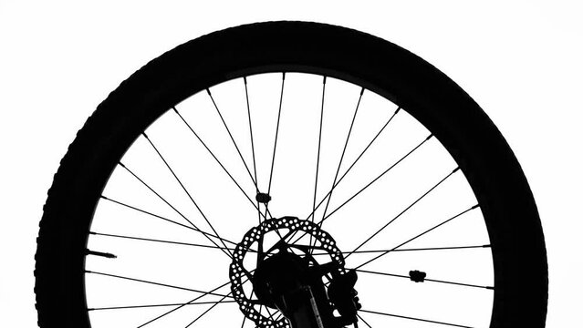 Black silhouette of a bicycle wheel spinning on a white isolated background. Close up of round bike wheel with rubber tread tire, spokes and brake. Rotation of the wheel on a sporty modern bike.