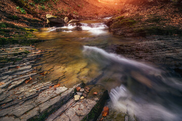 Amazing landscape mountain river in autumn forest at sunlight. View of stone water rapids and small waterfall.