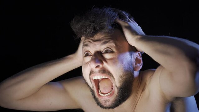 Mentally ill man going crazy and shouting.
Mentally deranged man screaming and going crazy in a dark room.
