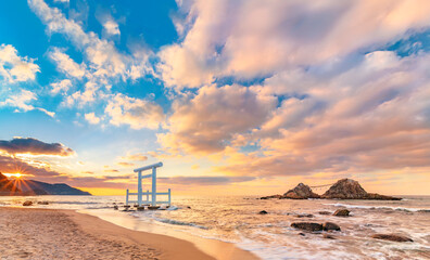 The sun setting on the horizon of the Itoshima Beach of Fukuoka where a white Shinto torii gate in...