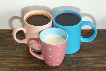 Three different ceramic mugs with different drinks - milk, coffee, fruit juice - on rustic table