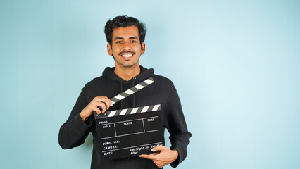 Cheerful Young Asian Indian man standing holding clapperboard, clapper board used in film making,...