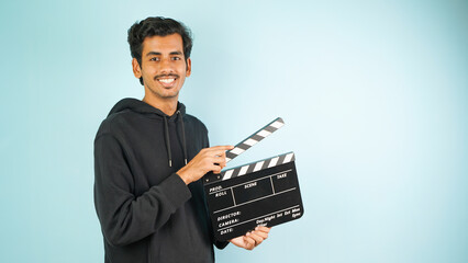 Cheerful Young Asian Indian man standing holding clapperboard, clapper board used in film making,...