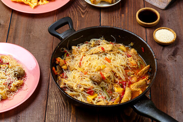 Funchoza with chicken and vegetables in teriyaki and oyster sauce in a frying pan on a covered wooden table.