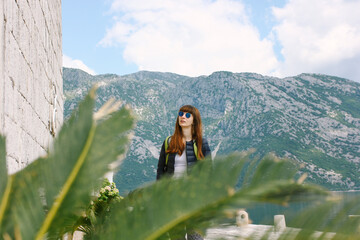 a young brunette girl in glasses, a tourist walks and looks at the sights, the old church against the backdrop of mountains