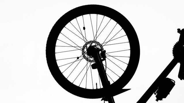 Black silhouette of a bicycle wheel spinning on a white isolated background. Close up of round bike wheel with rubber tread tire, spokes, bottle, pedals and brake. Rotation of the wheel on sporty bike