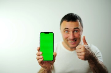 Advertising space for text A man with a green screen on the phone looks into the frame and shows a thumbs up Chroma key on the phone close to the camera white background white t-shirt on a man
