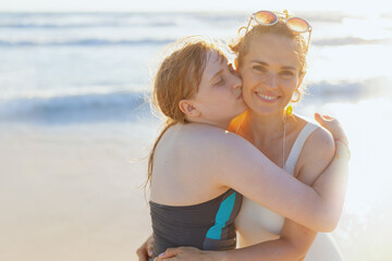 Portrait of smiling mother and teenage daughter at beach hugging