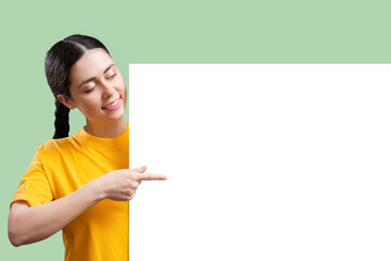 Digital advertisement. Happy young Caucasian woman points her finger at big placard with mock up, isolated on green background. Copy space. The concept of online shopping and social media