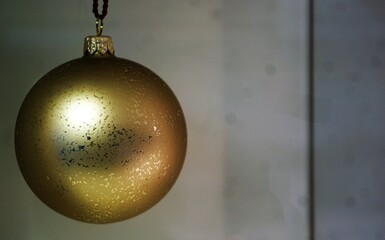 Dekoration mit goldgelber hängender Weihnachtskugel mit Licht vor weißer Wand 