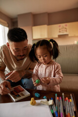Asian father looking at daughter with plasticine