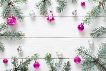 Fir branches and pink Christmas decorations on a white wooden background.