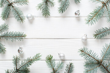 Fir branches with Christmas silver glass balls on a white wooden background.